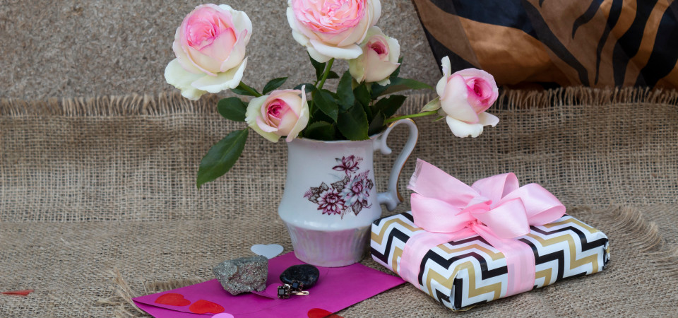 Ein hübsch verpacktes Geschenk liegt neben einer Vase mit rosa Blumen