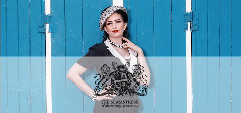 Eine Frau trägt ein schwarz-weißes Kleid und einen Hut im 40er Jahre Stil, Logo der Marke Seamstress of Bloomsbury