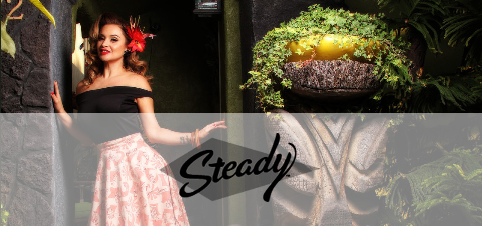 Eine Frau trägt ein 50er Jahre Outfit im Tiki-Style, Logo der Marke Steady Clothing