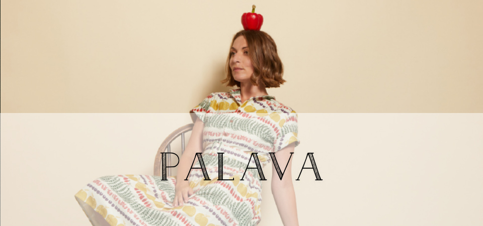 Eine Frau in einem Kleid mit Gemüse-Muster balanciert einen Apfel auf dem Kopf, Logo der Marke Palava