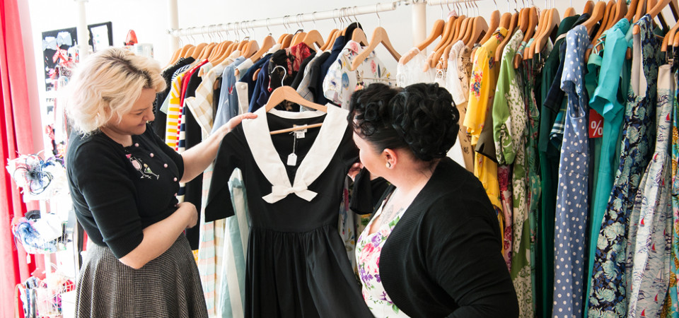 Eine Verkäuferin in einem Modegeschäft zeigt einer Kundin ein Kleid im Vintage-Stil