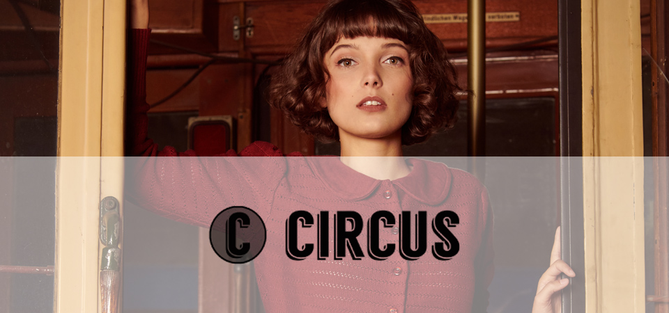 Eine dunkelhaarige junge Frau trägt eine weinrote Strickjacke im 50er Jahre Stil, Logo der Marke Circus